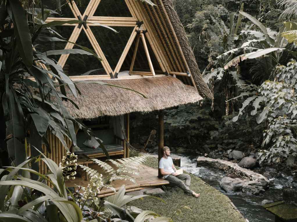 Two-story bamboo hospitality villa with a thatched roof beside a tropical river